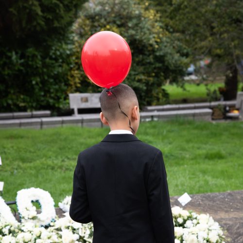 young boy carrying balloon looking at flower tributes at a funeral service