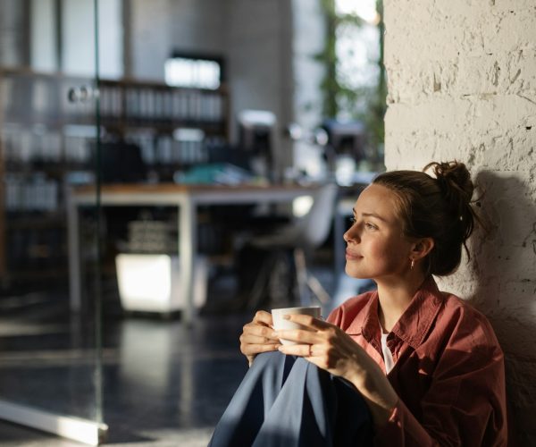 Happy female business owner in her own office drinking coffee and watching sunset.